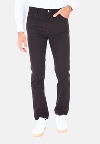 Pantaloni in misto cotone neri con dettagli di cucitura, design attillato e tasche anteriori. Indossati con sneakers bianche e una maglietta di colore chiaro.