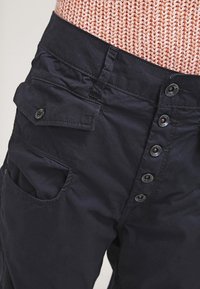 Granatowe spodnie cargo wykonane z tkaniny o gładkiej fakturze, z zapięciem na guziki, wieloma guzikami oraz detalem bocznej kieszeni.