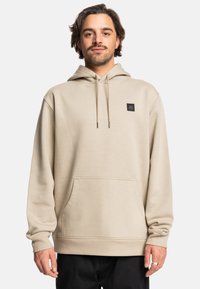 Licht beige hoodie met een voorzak, capuchon met koord en een zwart logo-opdruk op de borst. Zachte, gestructureerde stof, relaxte pasvorm.