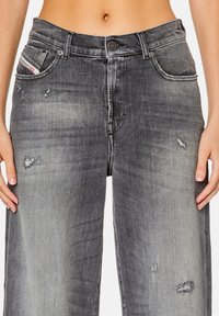 Tummanharmaat leveät farkut, joissa on kulutettuja yksityiskohtia, viisi taskua ja nappikiinnitys. Ominaisuuksiin kuuluu haalistunut ulkonäkö ja näkyvät saumat.