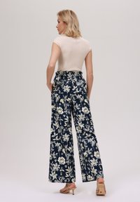 Blomstrede vide bukser med marineblå bunn, prydet med et hvitt blomsterdesign og smock-fasong på midjen. Brukt sammen med en tettsittende beige topp og hæler.