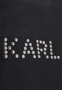 Sac en cuir noir avec le nom "KARL" formé de clous ronds en argent, présentant une surface texturée et un design moderne.