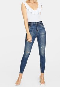 Vit bodysuit med volangkrage, kombinerad med högmidjade blå skinny jeans som har lätt slitna detaljer och en mjuk yta.
