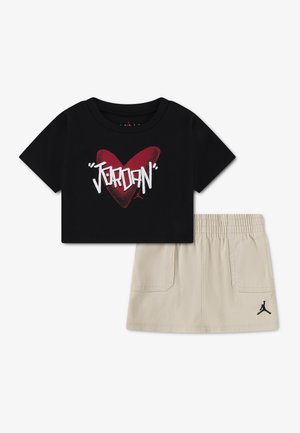 Sort kortærmet t-shirt med rødt hjerte og hvid "Jordan"-tekst, kombineret med beige nederdel med elastik i taljen og sort Jumpman-logo.
