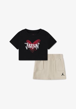 Czarny przycięty t-shirt z czerwonym sercem i białym napisem „Jordan” w zestawie z beżową spódnicą z elastyczną talią i czarnym logo Jumpman.
