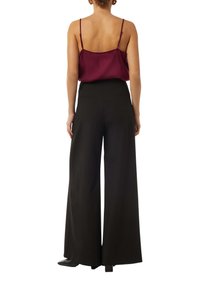 Black wide-leg pants with a smooth, flowing fabric, paired with a burgundy satin camisole featuring thin straps. Back view.