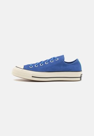 Sneakers blu in suede a taglio basso con suola in gomma bianca, striscia nera e occhielli in metallo. Dettaglio verde sul tallone. Design classico con punta rinforzata.