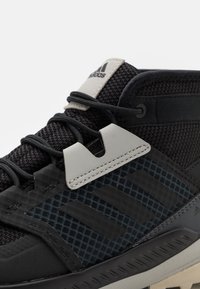 Černá sportovní obuv s texturovaným svrškem, šedými akcenty a logem se třemi pruhy. Šňůrky a gumová podešev zvyšují funkčnost.