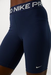 Nike Pro-shorts, marinblå, tillverkade av stretchigt material, har ett brett midjeband med "PRO" i ljusgrått, liten silverfärgad swoosh-logotyp.