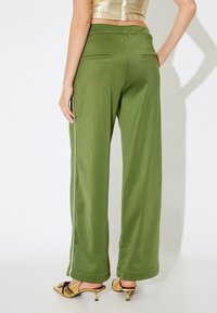 Olijfgroene wijde pantalons met een soepele textuur, voorzien van een witte zijstreep en twee achterzakken. De boorden zijn opgerold.