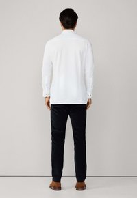Witte blouse met lange mouwen en puntkraag, met knoopmanchetten, rechte snit, gecombineerd met donkere broeken en bruine schoenen.