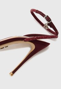 Burgundy high-heeled shoe with a suede finish, pointed toe, and a sparkling red strap featuring a buckle detail.