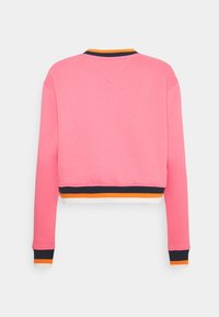 Oříznutá růžová mikina s výstřihem do V, kontrastní žebrované manžety s námořnickými, oranžovými a bílými pruhy na spodním lemu.