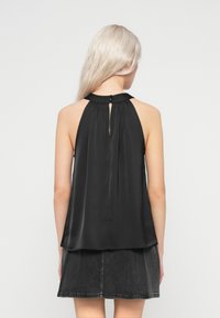 Mulher loira vestindo um top preto sem mangas com decote em gota e fechamento de botão, combinado com uma saia mini de denim escura.