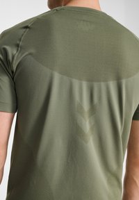 Oliwkowa zielona sportowa koszulka z krótkim rękawem, z fakturowanymi panelami z siateczki z tyłu i subtelnym wzorem szewronu w jaśniejszym odcieniu.