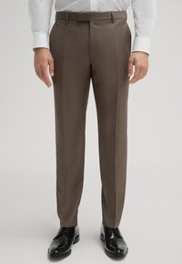 Braune Anzughosen mit glatter Textur, taillierter Passform und scharfer Bügelfalte. Getragen mit einem weißen Hemd und schwarzen Schuhen.