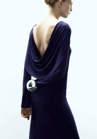 Głęboka niebieska sukienka z zamszowym tyłem, z gładkim, okrągłym srebrnym akcentem trzymanym w talii. Miękka, zwiewna faktura tkaniny.