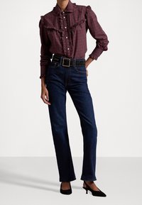 Röd och svart rutigt skjorta med volangkrage och knappar, kombinerat med mörkblå denimjeans och svarta spetsiga klackar.