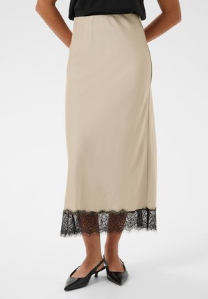 Jupe midi beige avec bordure en dentelle noire à l'ourlet, portée avec des escarpins slingback noirs à bout pointu et un top noir rentré.