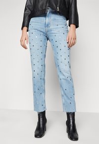 Ljusblå denimjeans med silverfärgade metallnitar i ett prickigt mönster, med råa fållar och rak benmodellen, bärs tillsammans med svarta ankelstövlar.