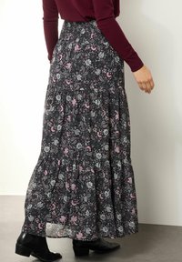 Zwarte maxi rok met bloemenmotief en een gelaagd ontwerp, met roze en witte patronen. Elastische tailleband en lichte stof.