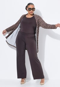 Bruine jumpsuit met een cardigan met luipaardprint, voorzien van lange mouwen en een open voorkant. Beige hakken maken de outfit compleet.