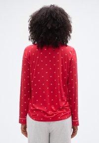 Κόκκινο τοπ με μακριά μανίκια, μικρό σχέδιο φιόγκου, φτιαγμένο από απαλό ύφασμα. Διαθέτει άνετη εφαρμογή και ελαφρώς καμπυλωτό τελείωμα. Μανσέτες με διακοσμητική λεπτομέρεια.