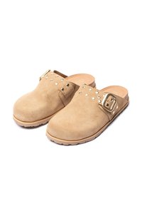 Tan suède klompen met een ronde neus, decoratieve studs en een metalen gespaccent. Contrasterende bruine hak en rubberen zool voor grip.