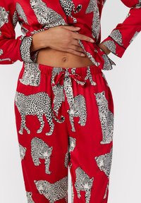 Red pajama set featuring a pattern of black and white leopards. Satin material with long sleeves and an elastic waistband.