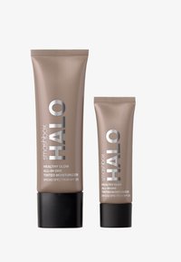 Dos tubos de cosméticos beige, uno grande y uno pequeño, etiquetados como "smashbox Halo Healthy Glow All-in-One Tinted Moisturizer," con bases negras.