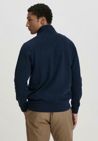 Dunkelblauer Sweatshirt mit hochgeschlossenem Kragen, langen Ärmeln und gerippten Bündchen sowie Saum. Hergestellt aus weichem Stoff mit matter Textur.