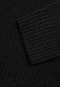 Primo piano di tessuto nero lavorato a maglia con polsino a coste che si sovrappone a uno sfondo lavorato a maglia testurizzato.