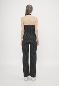 Svartstripet jumpsuit med halterneck og vid benklipp. Laget av et glatt stoff; har en tettsittende overdel og baklommer.