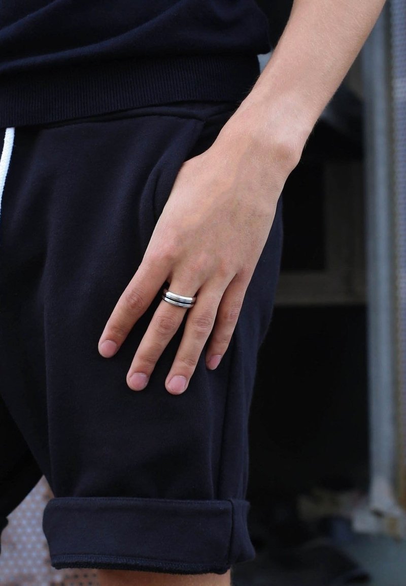Zwarte sportshorts met opgerolde mouwen; hand die op de zak rust. Metalen ring met meerdere ringen, die de cirkelvorm en gepolijste afwerking laat zien.