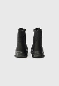 Melnu potītes zābaku ar teksturētu virsmu, aizdari aizmugurē, mīkstu apkakli un masīvu gumijas zoli, kas nodrošina atbalstu un izturību.