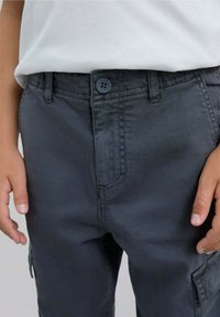 Pantalones cargo grises de algodón, con cierre de botón, bolsillos frontales y laterales, y detalles cosidos a lo largo de las costuras.