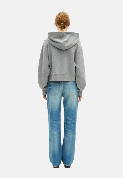 Felpa grigia corta con un ampio cappuccio e vestibilità rilassata, abbinata a jeans a gamba larga sbiaditi di color blu con un classico design a 5 tasche.