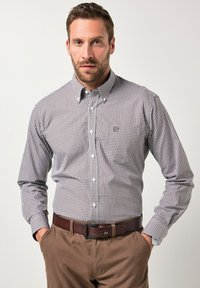 Camisa de botonadura en un patrón de cuadros marrón y blanco; cuenta con un cuello extendido, bolsillo en el pecho y mangas largas, combinada con pantalones marrones y un cinturón.
