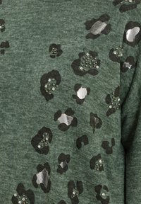 Tissu vert foncé avec des taches de léopard noires et argent métallisé, agrémenté de petites clous ronds en argent.