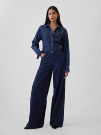 Tricou din denim închis cu nasturi și mâneci lungi, asortat cu pantaloni largi din denim închis. Textură netedă, croială ajustată, accente minime.