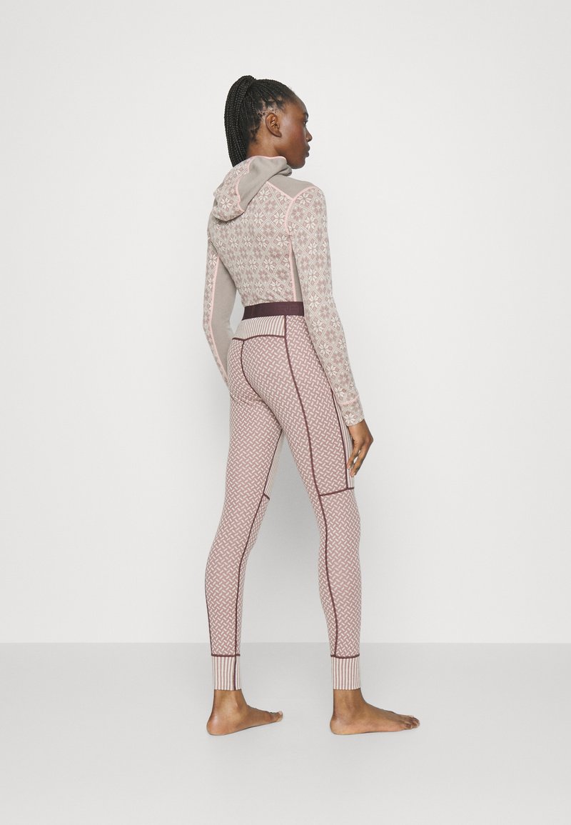 Ein gemustertes, tailliertes Sportensemble bestehend aus einem Kapuzenoberteil und Leggings in sanftem Beige und pastellrosa, mit kontrastierenden Details und Texturen.