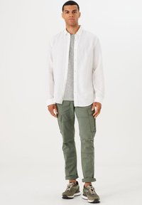 Camisa de lino blanca, camiseta gris, pantalones cargo oliva con bolsillos y zapatillas oliva y negras. Diseño simple, corte casual.