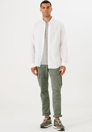 Camisa de lino blanca, camiseta gris, pantalones cargo oliva con bolsillos y zapatillas oliva y negras. Diseño simple, corte casual.