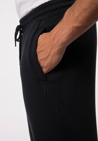 Schwarze Jogginghose aus weichem Stoff, mit einem elastischen Bund und einem Kordelzug, seitlichen Taschen und einem kleinen Logo-Detail.