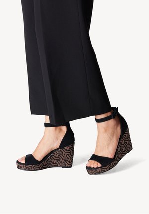 Sorte kilehæls-sandaler med ankelrem, med en tekstureret brun sål i geometrisk mønster og en glat ruskindsoverdel.