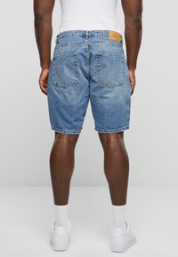 Shorts en denim de couleur bleu clair, dotés d'un tissu texturé, de cinq poches et d'une étiquette en cuir à l'arrière de la taille. Finition avec une coupe droite.