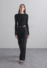 Black ribbed long-sleeve top paired with high-waisted black jeans featuring a decorative silver belt. Worn with black open-toe sandals.
