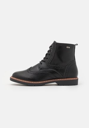 Bottine en cuir noir avec détails brogue, fermeture à lacets sur le devant, semelle cousue marron et languette à tirer sur fond blanc.