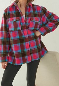 Fleece košile bunda v odvážném růžovém, fialovém a tyrkysovém kostkovaném vzoru, má dvě náprsní kapsy a zapínání na knoflíky, s volným střihem.