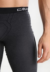 Leggings atléticos negros con textura acanalada, que cuentan con una cintura negra con un logo blanco y detalles de rayas blancas en los laterales.
